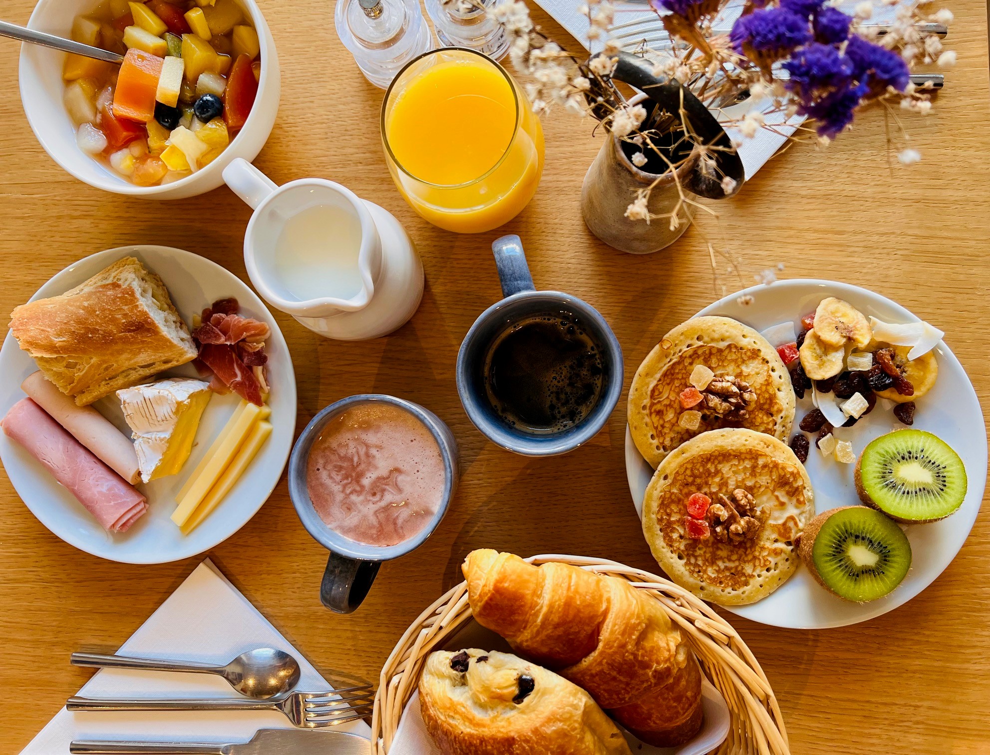 Table dressée pour le petit déjeuner avec une salade de fruit, pancakes, jambon, fromage, un verre de jus d'orange et deux tasses de café 